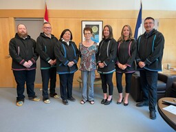 Clerks posing with artist in Gwich'in style robes. The Clerks wore these robes for the first time in the Chamber on May 30, 2023. From left to right, Michael Ball (Deputy Clerk - House Procedures and Committees), Glen Rutland (Clerk of the Legislative Assembly), Cynthia James (Committee Clerk), Ann Firth-Jones (artist), Amy Lizotte (Manager, Committees/Clerk of Journals), Kim Wickens (Deputy Clerk - Members' and Precinct Services), Frederick Blake, Jr. (Speaker)