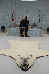 Paige Hawthorn (Youth Parliamentarian MLA Kam Lake) and Harjot Sidhu, Manager, Committees standing behind the Mace. Polar bear rug in foreground.