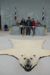 Jacee Mariano (Youth Parliamentarian MLA Range Lake) standing behind the Mace. Polar bear rug in foreground.