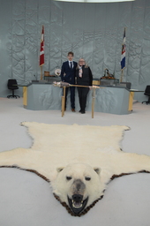 Hunter Groenewegen (Youth Parliamentarian MLA Hay River North) and Jane Groenewegan (grandmother) former Member of the Northwest Territories Legislative Assembly standing behind the Mace. Polar bear rug in foreground.