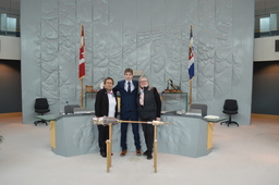 Northwest Territories Commissioner, Margaret Thom, Hunter Groenewegen (Youth Parliamentarian MLA Hay River North) and Jane Groenewegan (grandmother) former Member of the Northwest Territories Legislative Assembly standing behind the Mace. 