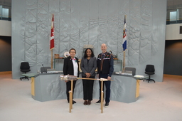 Northwest Territories Commissioner, Margaret Thom, Ritaj Hamad-Dawoud (Youth Parliamentarian MLA Yellowknife Centre) and Robert Hawkins, MLA Yellowknife Centre standing behind the Mace.